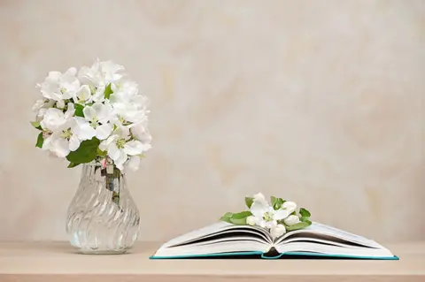 750opened-books-vase-with-white-flowers-table-against-background-wall