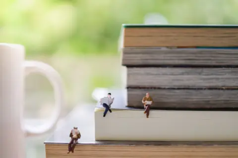 group-businessman-miniature-figure-sitting-reading-newspaper-book-stack-books-with-mug-cup-hot-coffee-1