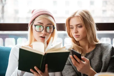 cheerful-two-women-friends-sitting-cafe-reading-book-1